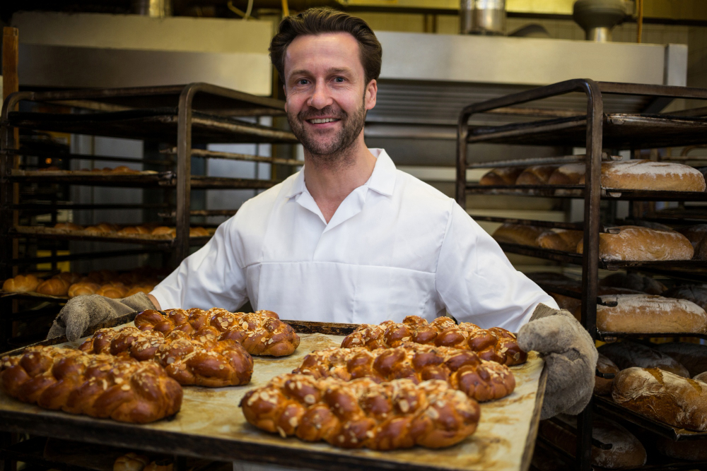 smiling-baker-holding-loaf-freshly-baked-twisted-buns